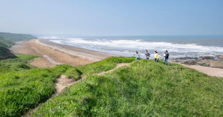 Family with 2 adults and 3 children walking on clifftop on Durham Heritage Coast with North Sea and beach in background